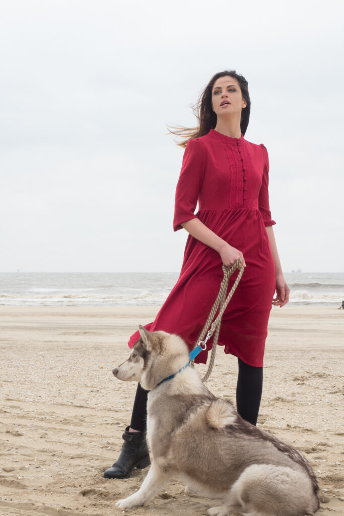 Model met rode jurk met Husky hond aan zee